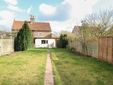 A garden with grass a stone path and a house with a tiled roof at Rose Cottage in Downham Market
