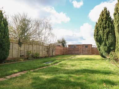 A fenced garden with green grass trees and a wooden shed at Rose Cottage in Downham Market
