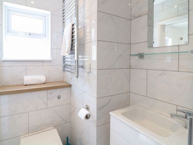 A bathroom with a toilet toilet paper towel rail sink cabinet mirror and a window at Pepperpots in Mawgan Porth