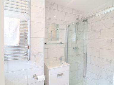 A bathroom with a shower enclosure a small sink a glass shelf a mirror a towel rail with a towel and a toilet paper holder at Pepperpots in Mawgan Porth