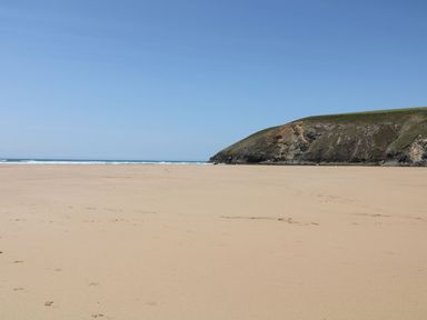 A sandy beach with a hill and ocean waves at Pepperpots in Mawgan Porth