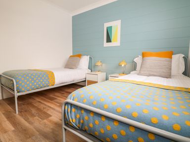 A bedroom with two single beds with blue and yellow polka dot blankets and bedside tables with lamps at Pepperpots in Mawgan Porth