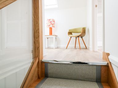 A stair with carpet leading to a room with a wooden chair and a side table with a lamp at Pepperpots in Mawgan Porth