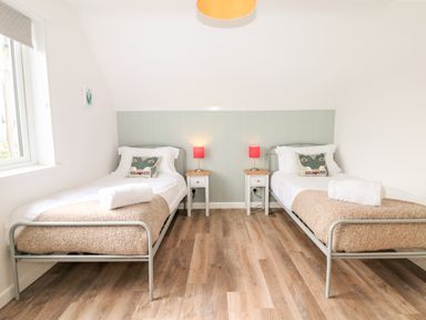 A bedroom with two single beds bedside tables with lamps and a window at Pepperpots in Mawgan Porth