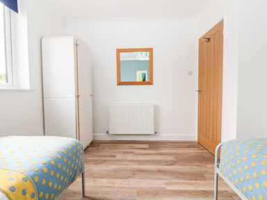A bedroom with two beds a wooden door a white wardrobe a wall-mounted radiator and a mirror at Pepperpots in Mawgan Porth