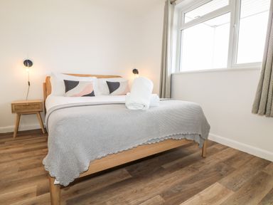 A bedroom with a wooden bed frame gray blanket pillows bedside table and window at Pepperpots in Mawgan Porth