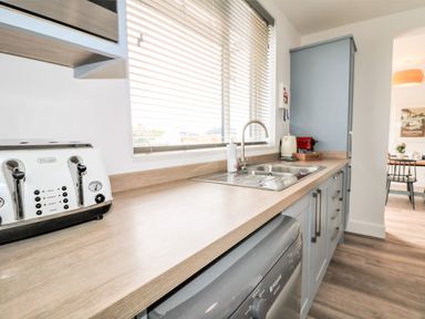A kitchen with a toaster sink and cabinets and a dining area visible through a doorway at Pepperpots in Mawgan Porth
