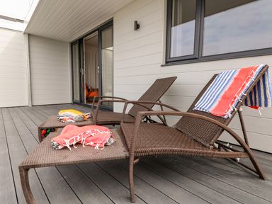 A patio with two brown wicker lounge chairs and folded towels on a gray deck at Pepperpots in Mawgan Porth