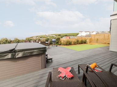 An outdoor patio area with a hot tub dining table chairs barbecue and lounge chairs at Pepperpots in Mawgan Porth