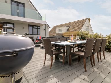 An outdoor patio with a dining table and chairs a barbecue and houses in the background at Pepperpots in Mawgan Porth