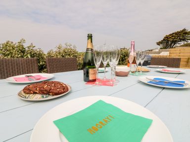 An outdoor table set with plates napkins glasses two bottles of champagne and a plate of cookies at Pepperpots in Mawgan Porth