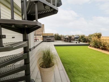 A backyard with a spiral staircase wooden deck with a hot tub dining table and a barbecue grill at Pepperpots Mawgan Porth
