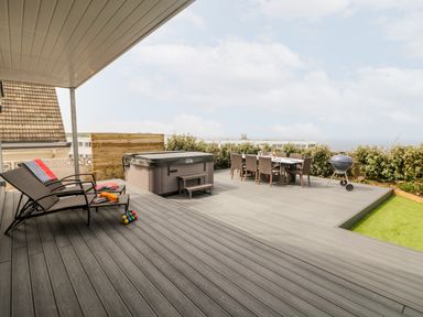 An outdoor patio with lounge chairs hot tub dining table and barbecue at Pepperpots in Mawgan Porth