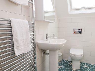 A bathroom with a pedestal sink a toilet a towel rail with a white towel and a skylight window at Pepperpots in Mawgan Porth