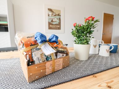 A gift basket with a blue bow next to a potted plant and cups on a wooden table at Pepperpots in Mawgan Porth