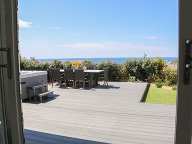 A wooden deck patio with a dining table and chairs a hot tub and ocean view at Pepperpots in Mawgan Porth