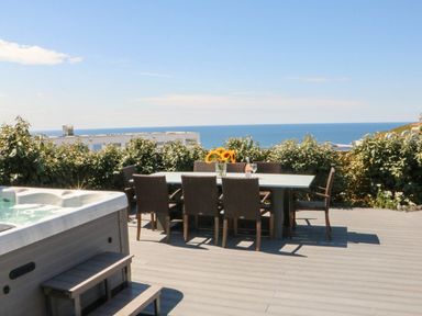 An outdoor dining table with chairs and a vase of sunflowers next to a hot tub on a deck with ocean view at Pepperpots in Mawgan Porth