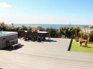 An outdoor patio with a dining table and chairs a hot tub a dog on grass and ocean view at Pepperpots in Mawgan Porth