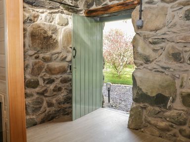An open green door in a stone wall showing a garden with a tree and a pathway at Bennar Fawr in Dyffryn Ardudwy
