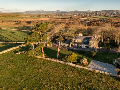 A stone house surrounded by trees and fenced grassy fields in a rural area at Bennar Fawr in Dyffryn Ardudwy