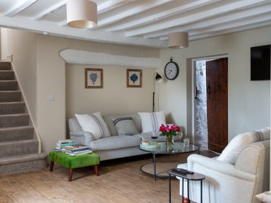 A living room with sofas a green ottoman with books a glass coffee table flowers and a clock on the wall at Bennar Fawr in Dyffryn Ardudwy