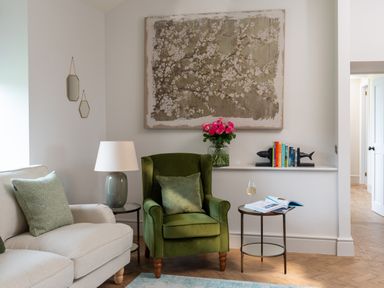 A living room with a green armchair beige sofa side tables a lamp flowers books and artwork at Bennar Fawr in Dyffryn Ardudwy