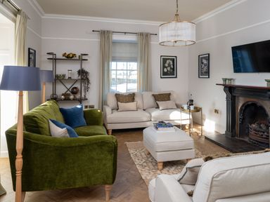 A living room with green and beige sofas a beige ottoman bookshelf fireplace and wall-mounted TV at Bennar Fawr in Dyffryn Ardudwy