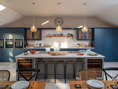 A kitchen with blue cabinets a white marble island with stools and pendant lights at Bennar Fawr in Dyffryn Ardudwy