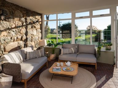 A sunroom with two sofas a woven coffee table with tea and cookies and plants at Bennar Fawr in Dyffryn Ardudwy