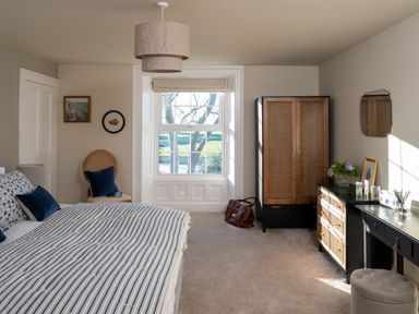 A bedroom with a bed with striped bedding a window a chair wardrobe dresser a desk and a round ottoman at Bennar Fawr in Dyffryn Ardudwy