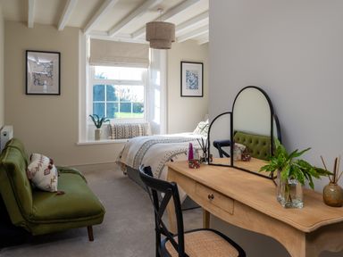 A bedroom with a bed, green sofa, wooden dressing table with mirror and a window with a cushion at Bennar Fawr in Dyffryn Ardudwy