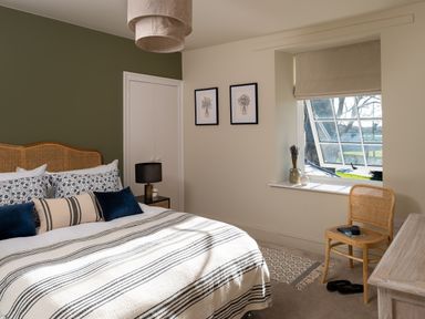 A bedroom with a striped bedspread and patterned pillows a chair near a window and two framed pictures on the wall at Bennar Fawr in Dyffryn Ardudwy
