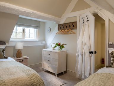 A bedroom with two beds a window a dresser with a mirror and flowers and robes hanging on a door at Bennar Fawr in Dyffryn Ardudwy
