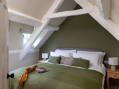 A bedroom with a green bedspread and pillows under white painted beams at Bennar Fawr in Dyffryn Ardudwy