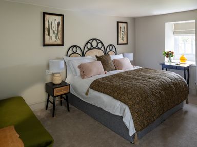 A bedroom with a double bed sides tables a window table with flowers and a green bench at Bennar Fawr in Dyffryn Ardudwy