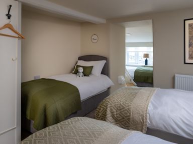 A bedroom with three single beds with green and beige blankets a stuffed bear and a window with a lamp at Bennar Fawr in Dyffryn Ardudwy