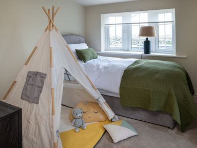 A bedroom with a bed next to a window and a small play tent with cushions and a teddy bear on the floor at Bennar Fawr in Dyffryn Ardudwy
