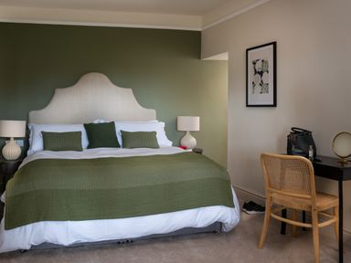 A bedroom with a large bed green blanket and pillows two bedside tables with lamps a wooden chair and a desk at Bennar Fawr in Dyffryn Ardudwy