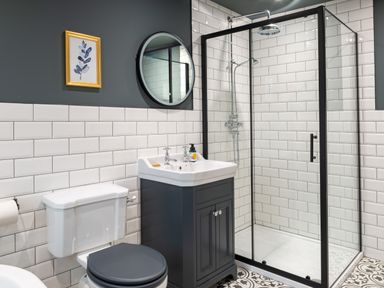 A bathroom with a white toilet black seat a sink with cabinet a glass shower enclosure and a round mirror at Bennar Fawr in Dyffryn Ardudwy