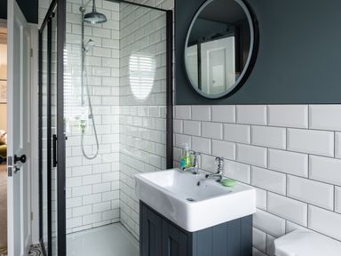 A bathroom with a glass shower enclosure white tiled walls a sink with two taps a round mirror and a soap dispenser at Bennar Fawr in Dyffryn Ardudwy