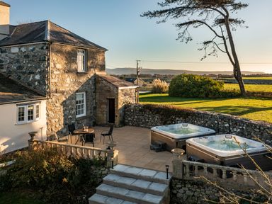 An outdoor patio with two hot tubs a table with four chairs stone walls and a stone house at Bennar Fawr in Dyffryn Ardudwy