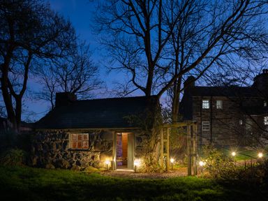A stone cottage with an open door and garden lights at Bennar Fawr in Dyffryn Ardudwy
