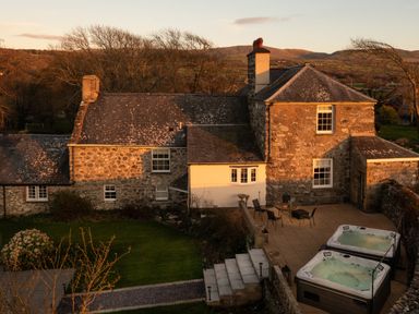 A stone house with a patio area containing two hot tubs and outdoor furniture at Bennar Fawr in Dyffryn Ardudwy
