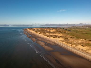 A beach with sand dunes and water beside grassy land and mountains in the distance at Bennar Fawr in Dyffryn Ardudwy