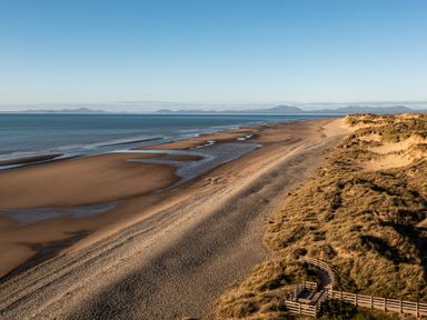 A sandy beach with water pools and grass-covered dunes near a wooden walkway at Bennar Fawr in Dyffryn Ardudwy