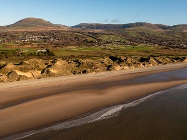 A sandy beach with waves and dunes with fields and hills in the background at Bennar Fawr in Dyffryn Ardudwy