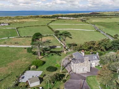 A stone house with a paved driveway near green fields fenced by stone walls and a sea view at Bennar Fawr in Dyffryn Ardudwy