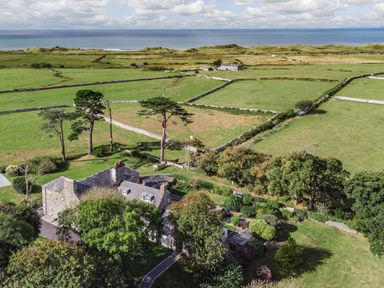 A stone house with trees and garden surrounded by green fields and stone walls near the coast at Bennar Fawr in Dyffryn Ardudwy