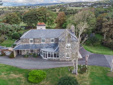 Stone house with slate roof surrounded by trees and lawn with a paved driveway at Bennar Fawr in Dyffryn Ardudwy