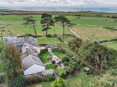 A house with gardens and trees near fields with stone fences and the sea in the background at Bennar Fawr in Dyffryn Ardudwy